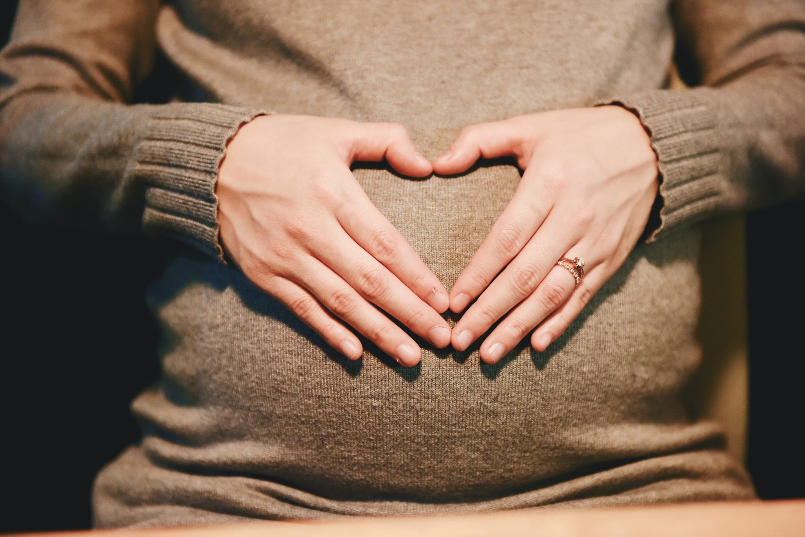 Pro-life bible verses: woman's hands cover her pregnant belly in the shape of a heart
