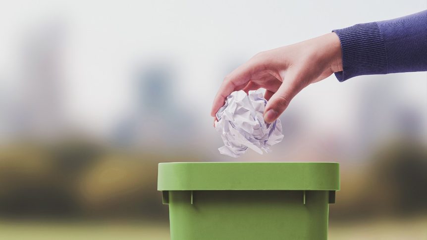 A white hand throwing balled-up paper into a green trash bin